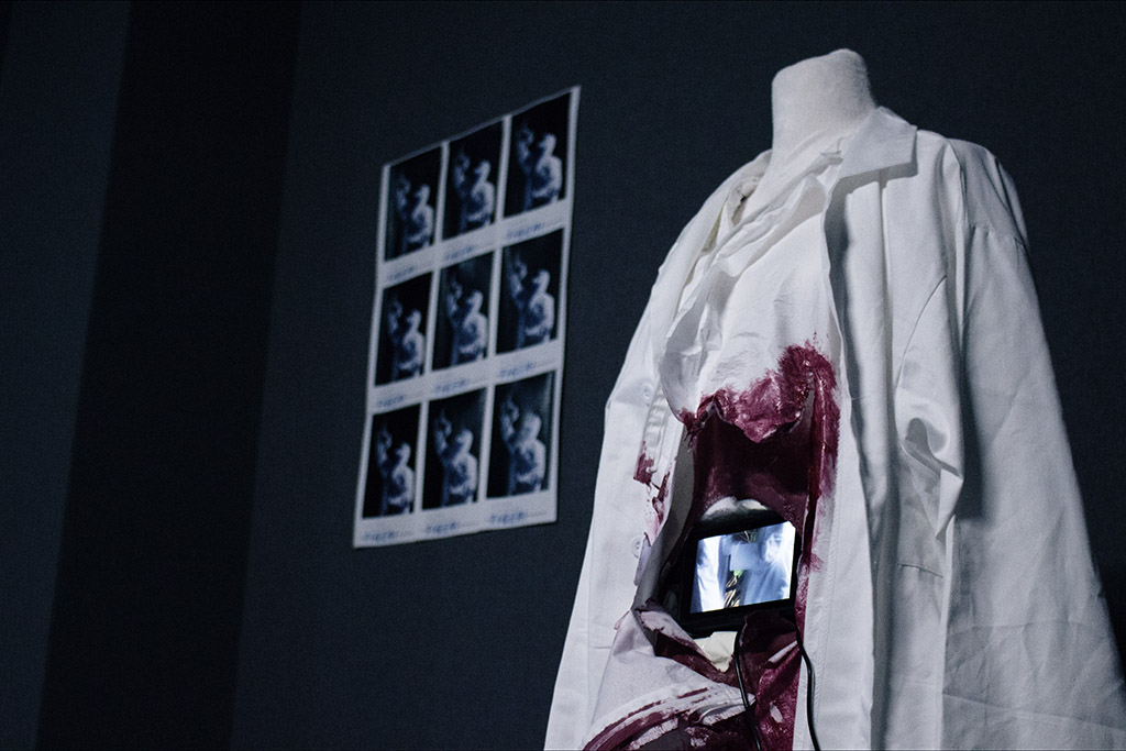 A video screen embedded in a bloody mannequin wearing a lab coat